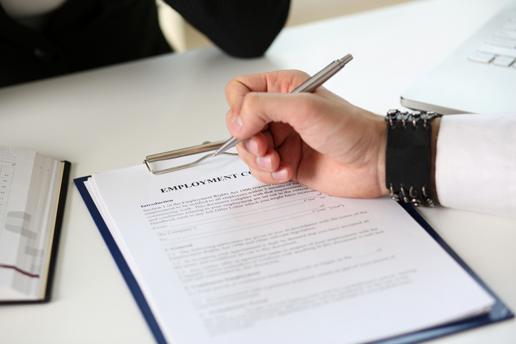 Male arm in office reading and signing employment contract form