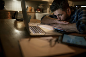 Photo of a stressed man going trough his financials problems,he is sitting in kitchen late at night checking and paying bills