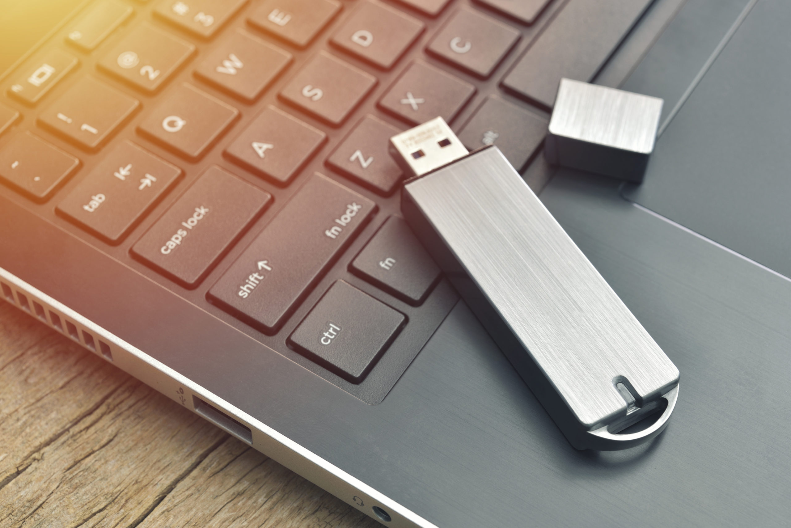 Close up of metal USB flash drive connected to laptop on wood desk