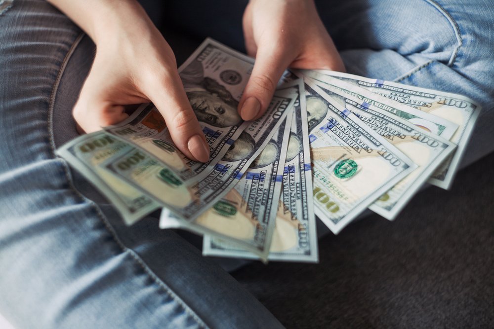 Hands holding one hundred dollar bills and fanning them out.