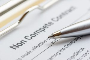 silver pen and a non compete contract on a clipboard.