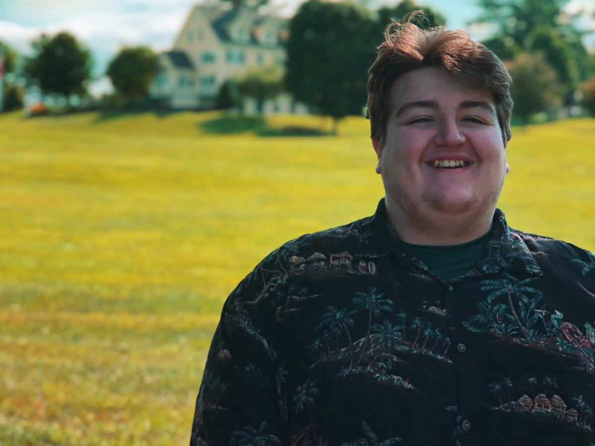 A man smiling in front of a house in a field.