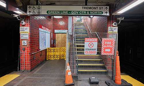Photo of stairs and elevators in Park Street station of the Red Line. Both areas are closed and have multiple signs of danger, warnings, and alarms. Orange cones on the front.