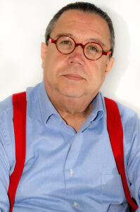 A headshot of Eduardo Aguado L&oacute;pez, a man wearing red circular glasses, a blue button up shirt, and red suspenders.