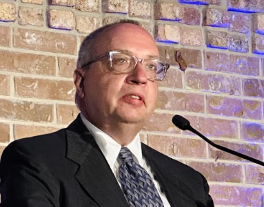 photo of Dennis speaking with a brick wall background