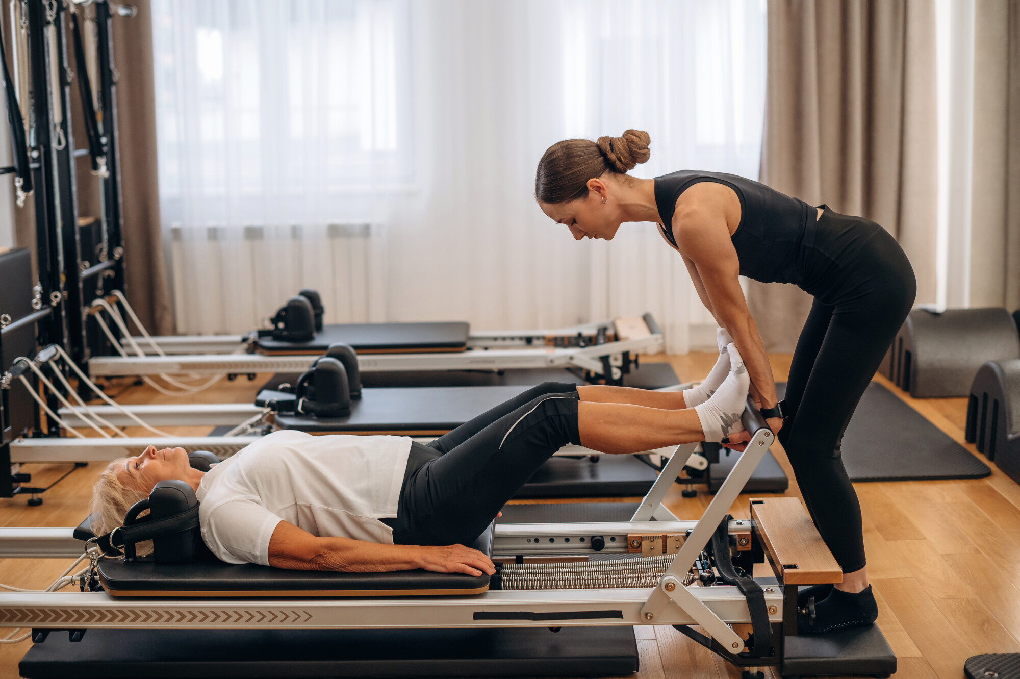 Elderly woman being helped by younger woman work out on fitness machine